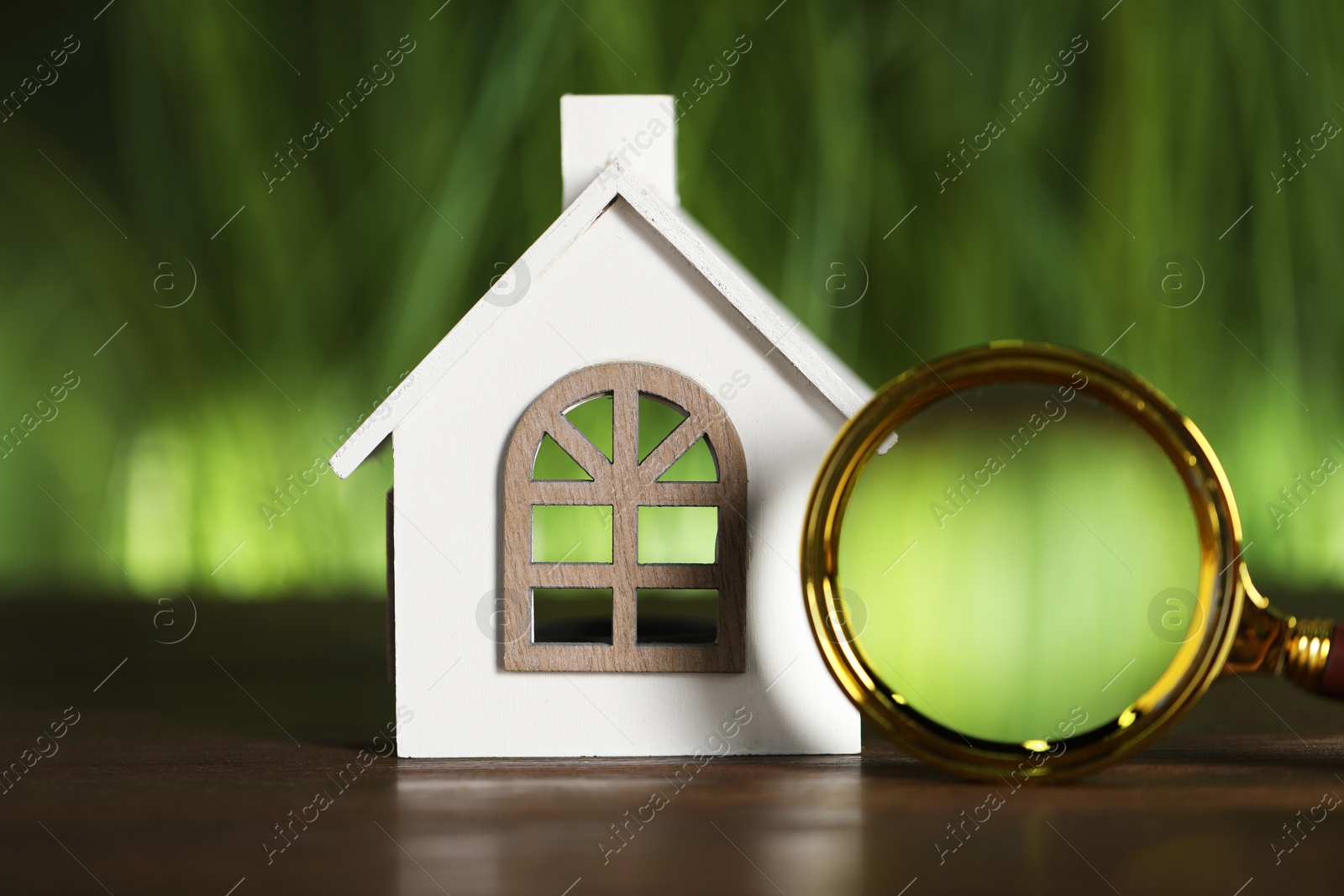 Photo of House hunting. Magnifying glass and house figure on wooden table