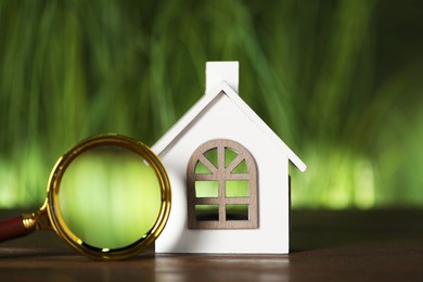 House hunting. Magnifying glass and house figure on wooden table