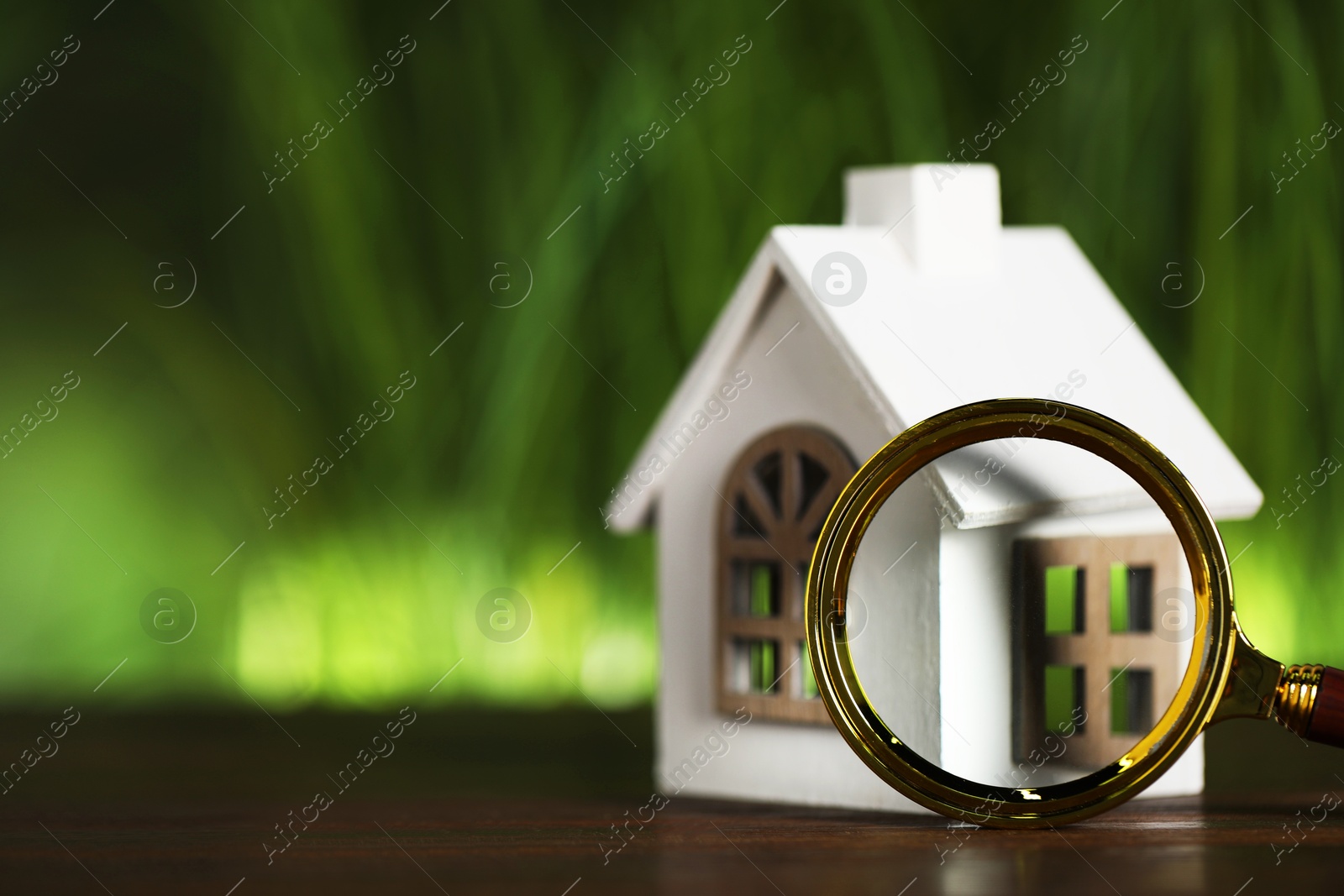 Photo of House hunting. Magnifying glass and house figure on wooden table, space for text