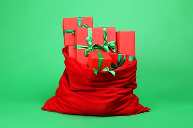 Photo of Red Santa Claus bag with gift boxes on green background