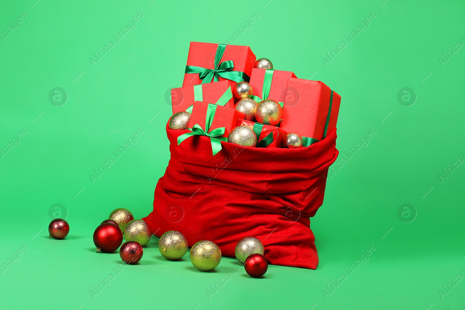 Photo of Red Santa Claus bag with baubles and gift boxes on green background