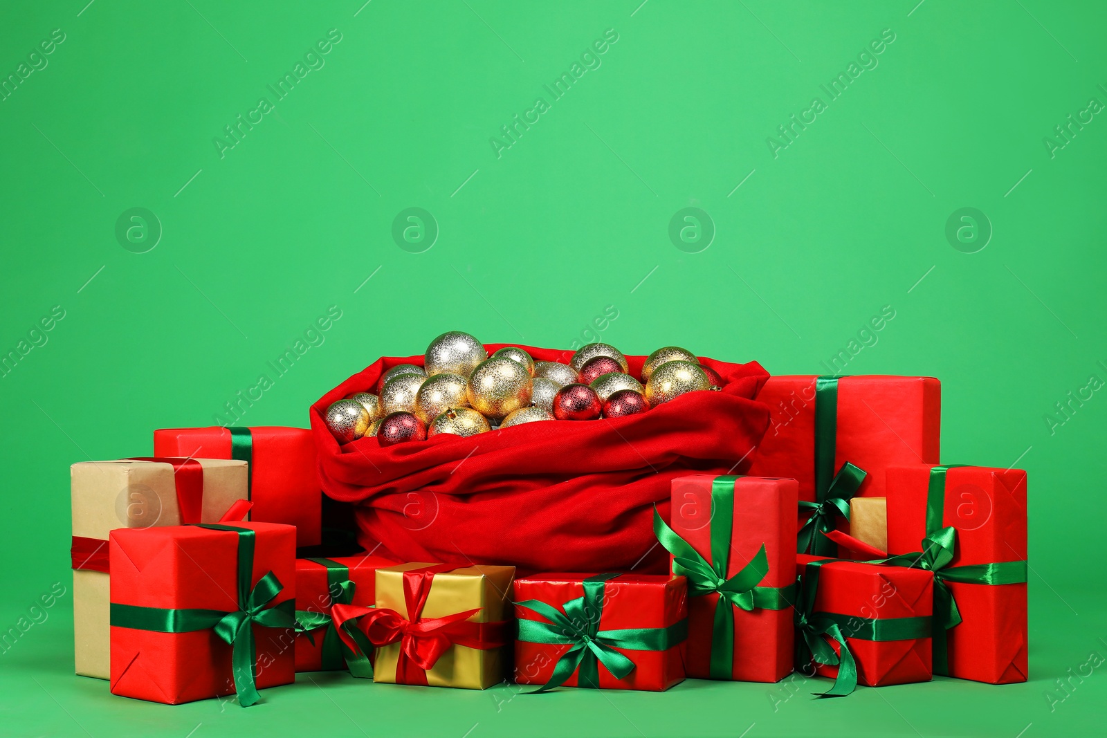 Photo of Red Santa Claus bag with baubles and gift boxes on green background