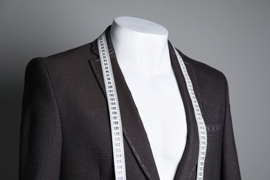 Photo of Semi-ready jacket with tailor's measuring tape on mannequin against grey background, closeup