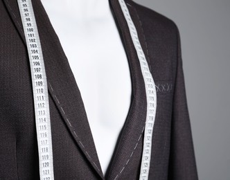 Semi-ready jacket with tailor's measuring tape on mannequin against grey background, closeup