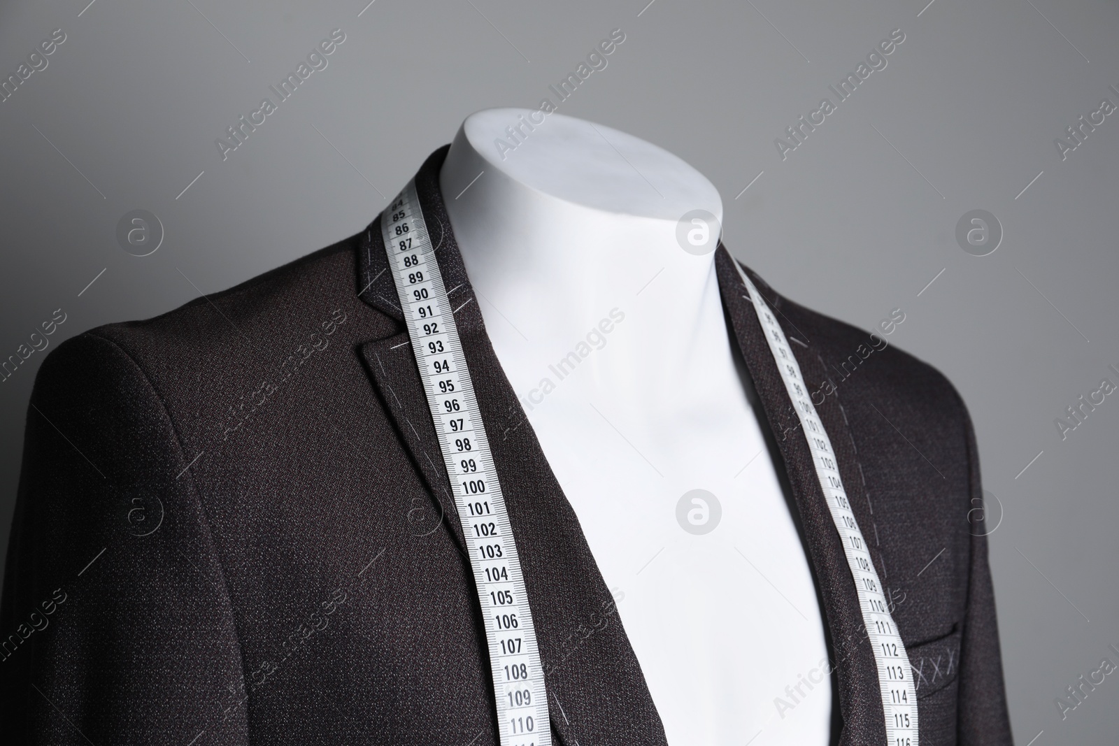 Photo of Semi-ready jacket with tailor's measuring tape on mannequin against grey background, closeup