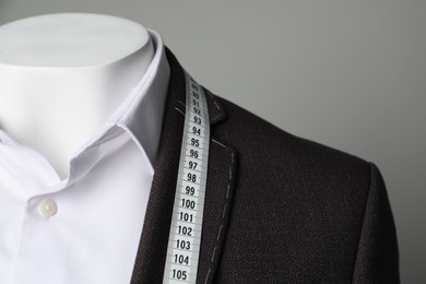 Photo of Semi-ready jacket with tailor's measuring tape and white shirt on mannequin against grey background, closeup