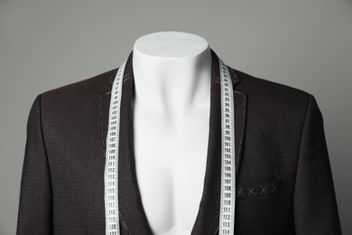 Semi-ready jacket with tailor's measuring tape on mannequin against grey background, closeup