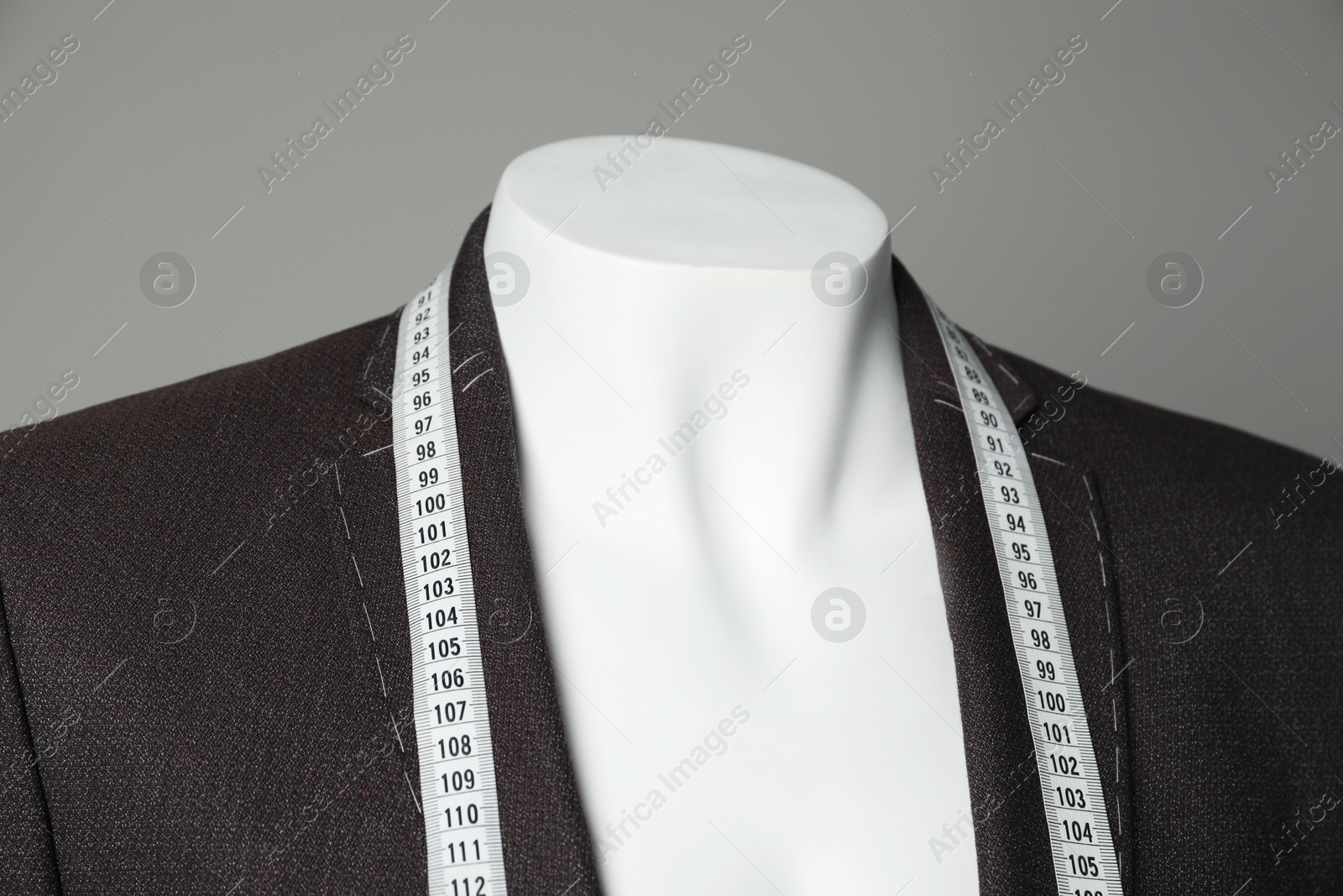 Photo of Semi-ready jacket with tailor's measuring tape on mannequin against grey background, closeup