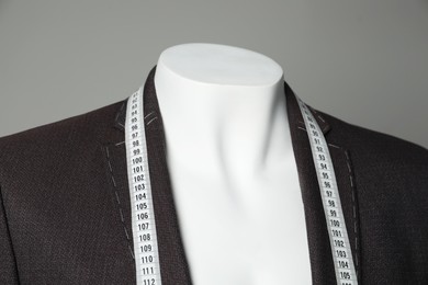 Photo of Semi-ready jacket with tailor's measuring tape on mannequin against grey background, closeup