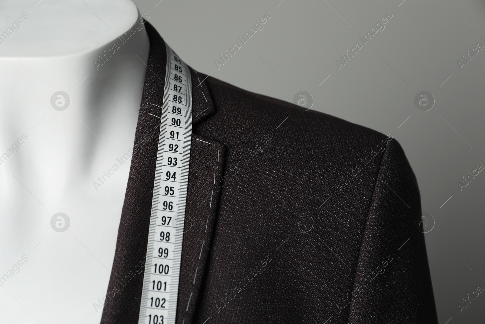 Photo of Semi-ready jacket with tailor's measuring tape on mannequin against grey background, closeup