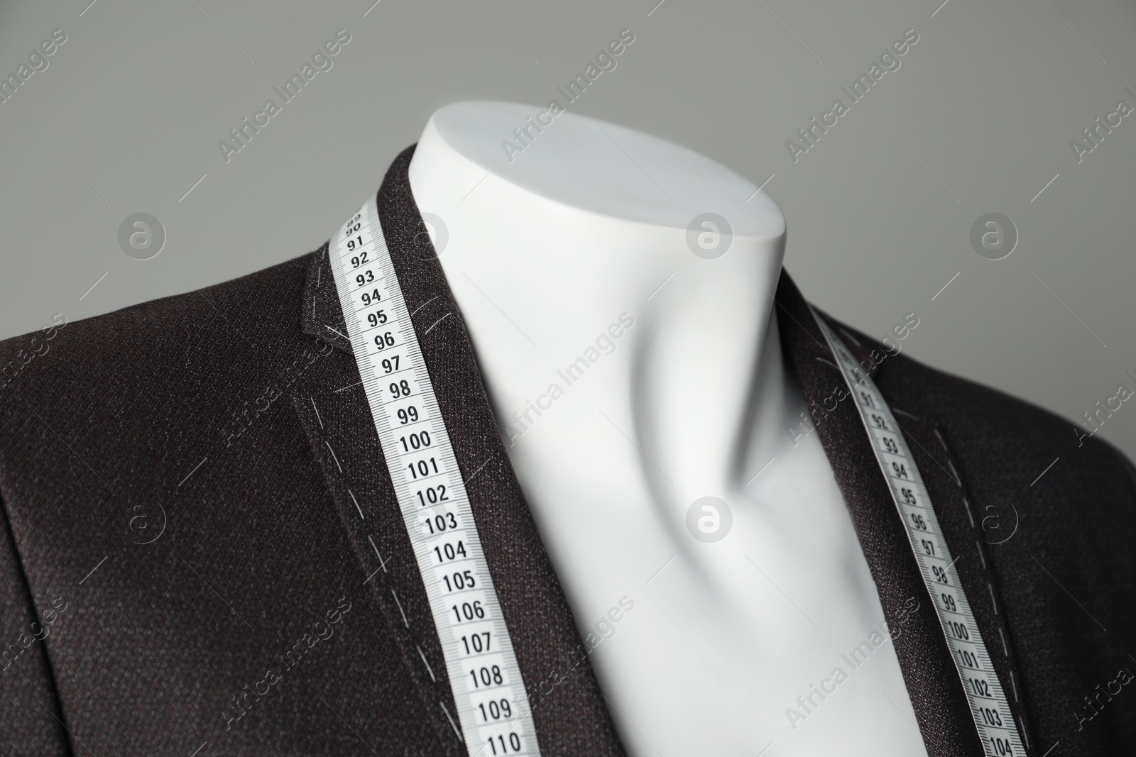 Photo of Semi-ready jacket with tailor's measuring tape on mannequin against grey background, closeup