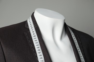 Photo of Semi-ready jacket with tailor's measuring tape on mannequin against grey background, closeup