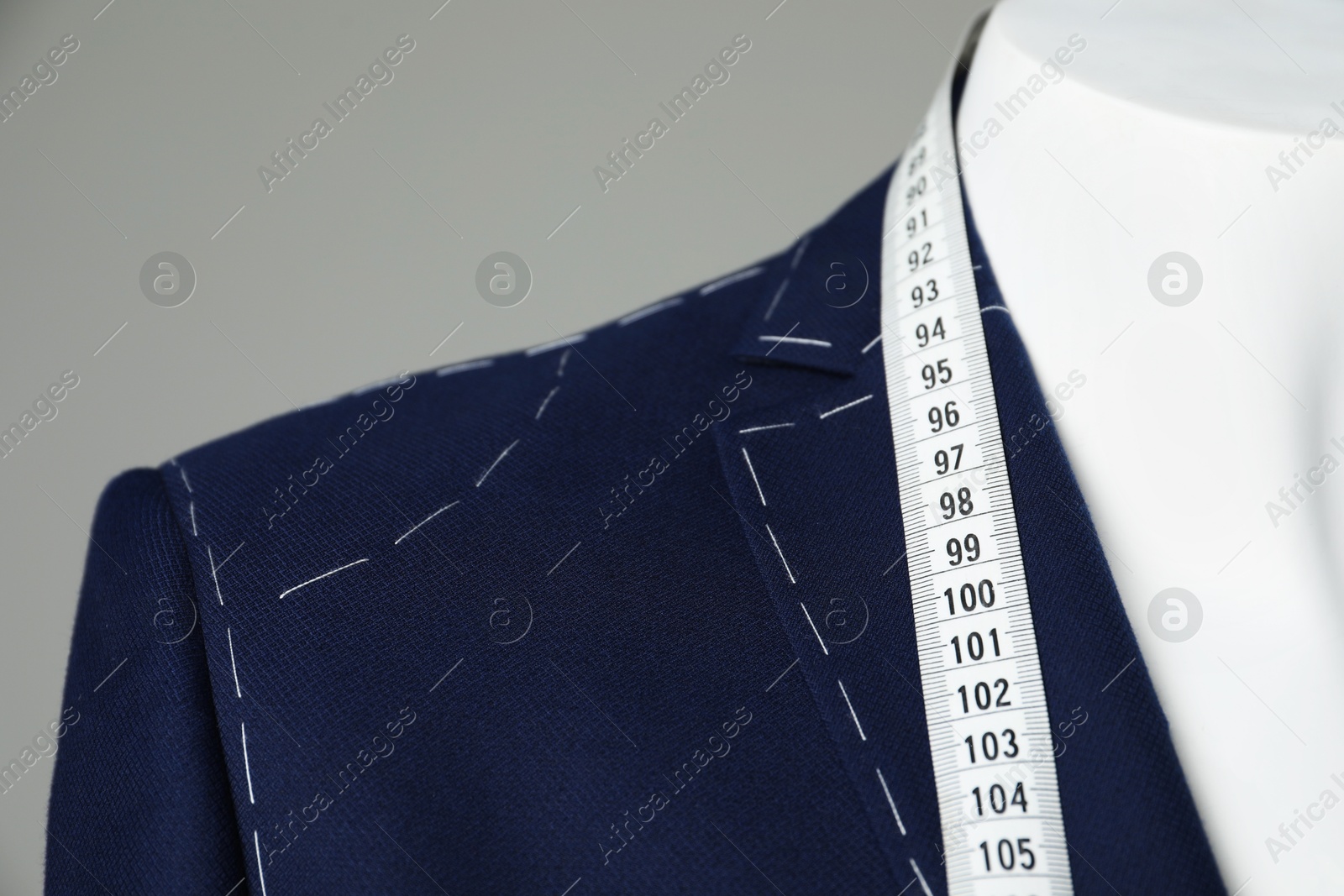 Photo of Semi-ready jacket with tailor's measuring tape on mannequin against grey background, closeup