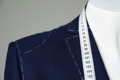 Photo of Semi-ready jacket with tailor's measuring tape on mannequin against grey background, closeup