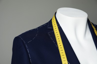 Photo of Semi-ready jacket with tailor's measuring tape on mannequin against grey background, closeup