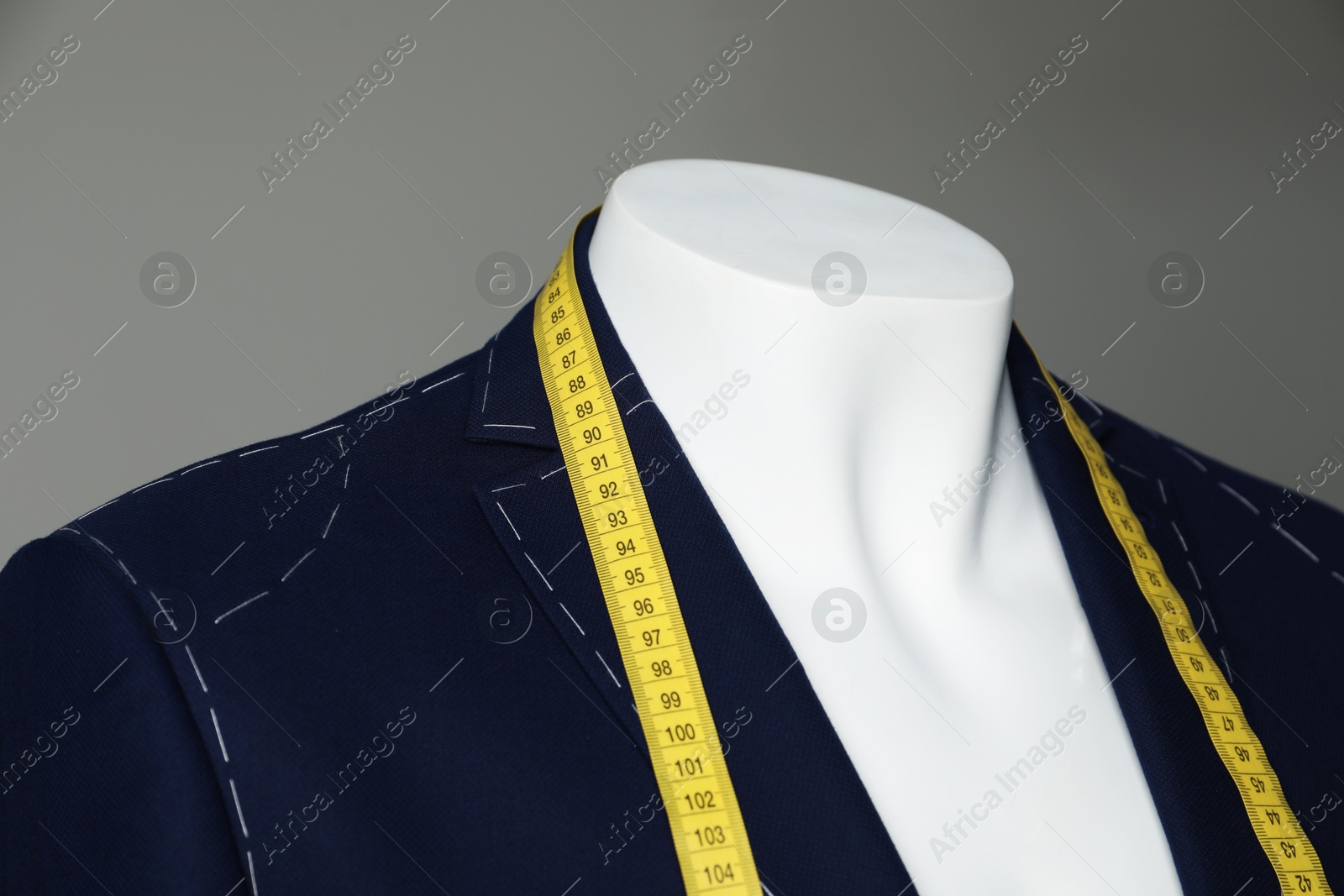 Photo of Semi-ready jacket with tailor's measuring tape on mannequin against grey background, closeup