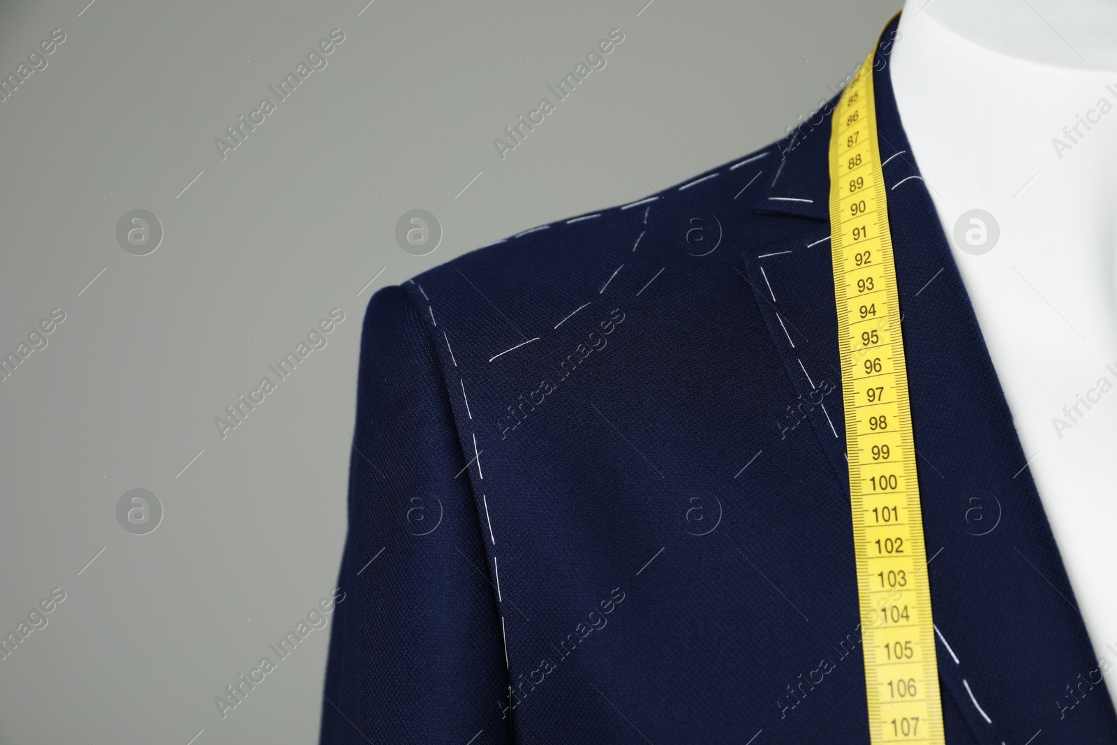 Photo of Semi-ready jacket with tailor's measuring tape on mannequin against grey background, closeup