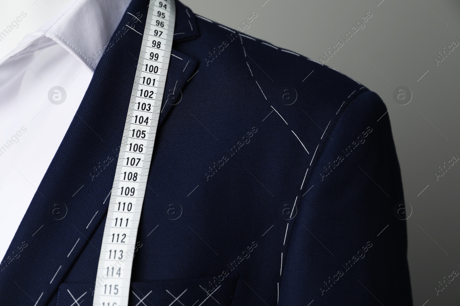 Photo of Semi-ready jacket with tailor's measuring tape and white shirt on mannequin against grey background, closeup