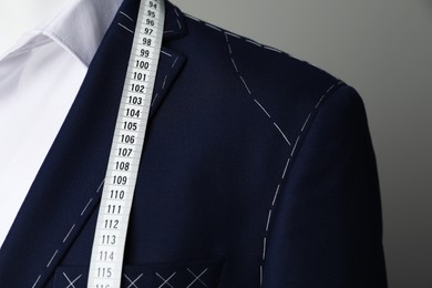 Photo of Semi-ready jacket with tailor's measuring tape and white shirt on mannequin against grey background, closeup