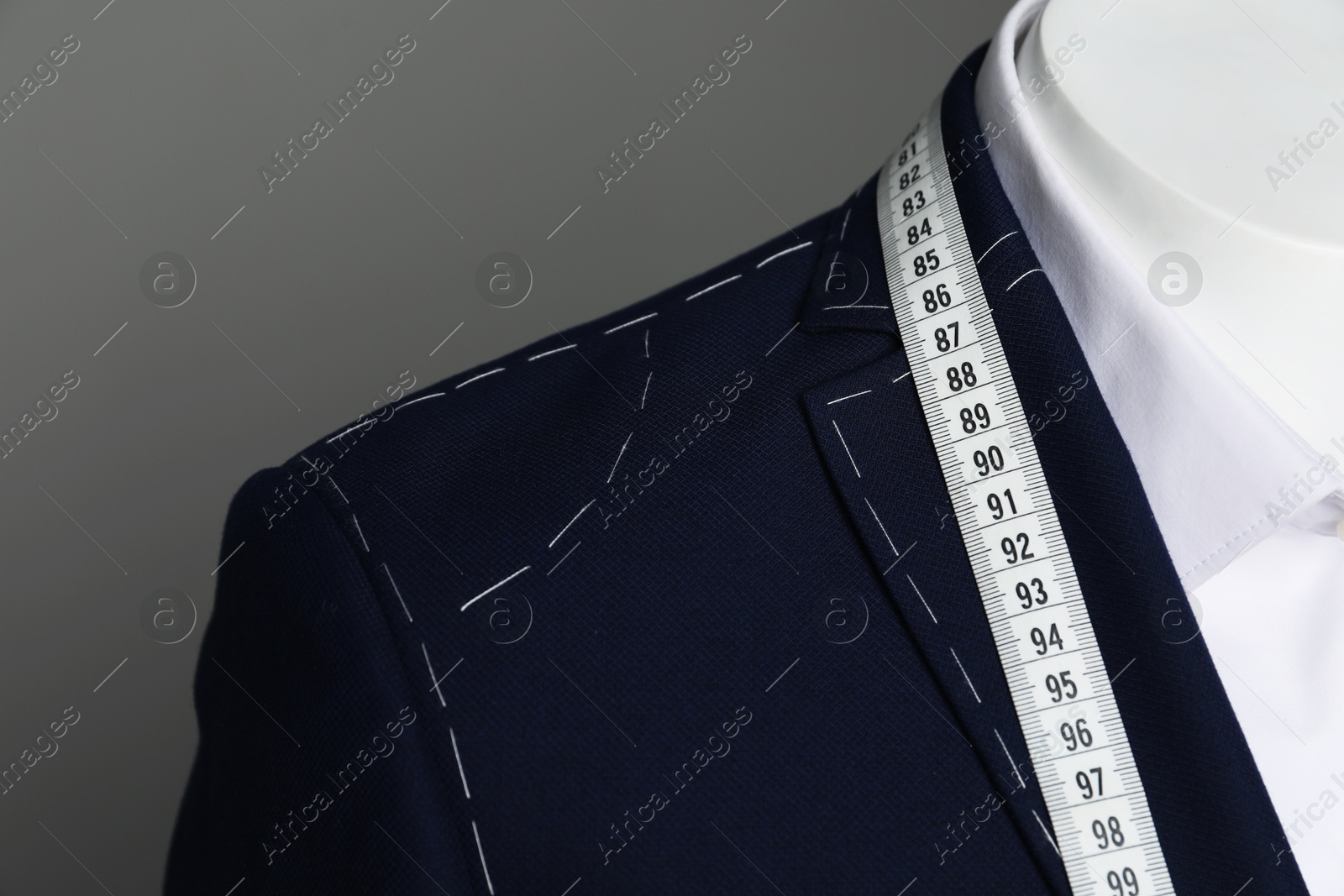 Photo of Semi-ready jacket with tailor's measuring tape and white shirt on mannequin against grey background, closeup