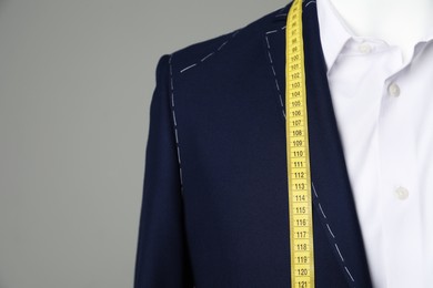 Photo of Semi-ready jacket with tailor's measuring tape and white shirt on mannequin against grey background, closeup