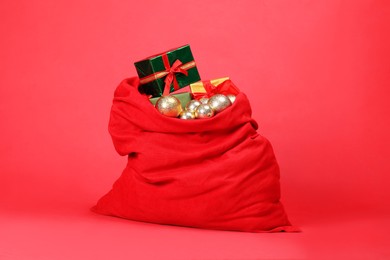 Photo of Santa Claus bag with baubles and gift boxes on red background