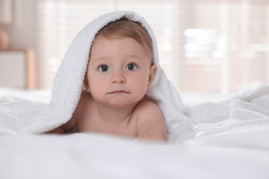 Photo of Cute baby under terry towel lying on bed at home