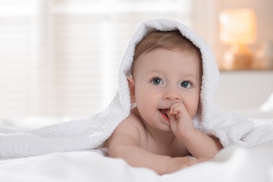 Photo of Cute baby under terry towel lying on bed at home