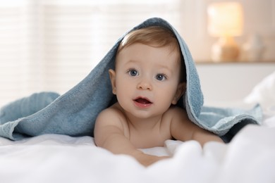 Photo of Cute baby under terry towel lying on bed at home