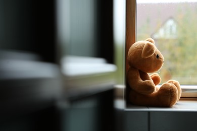 Photo of Lonely teddy bear near window on rainy day. Space for text