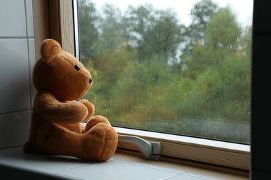 Photo of Lonely teddy bear near window on rainy day. Space for text