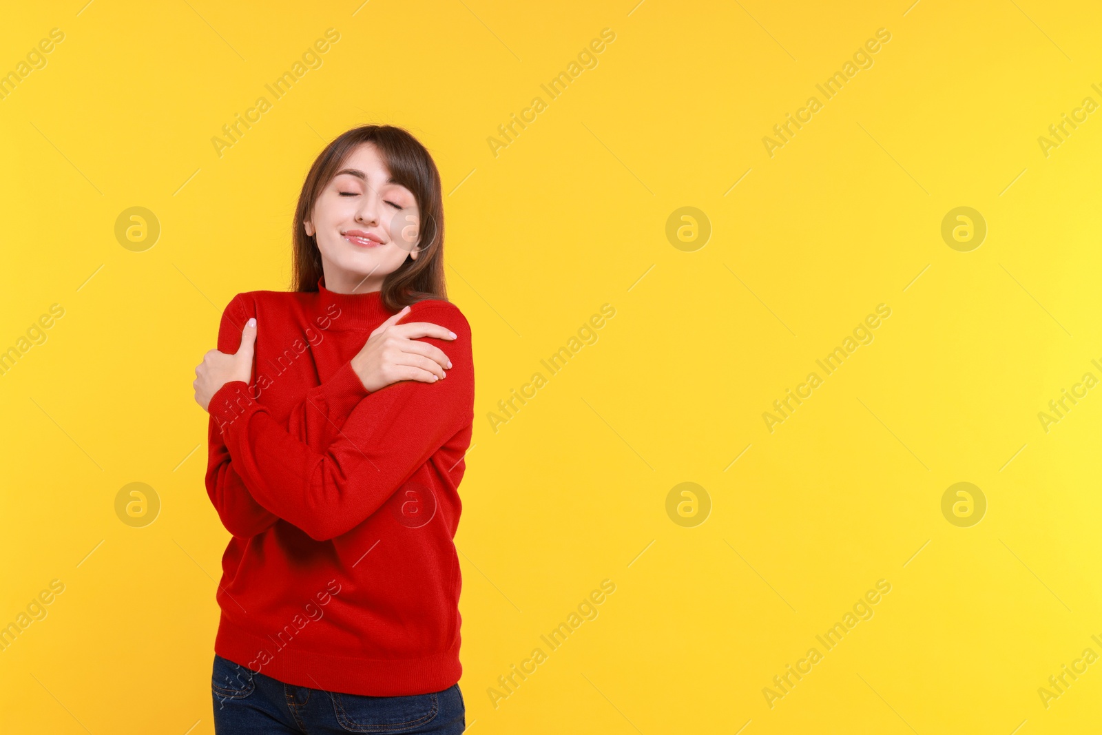 Photo of Young woman hugging himself on yellow background, space for text