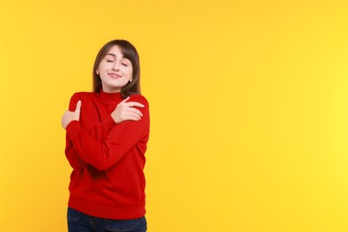 Photo of Young woman hugging himself on yellow background, space for text