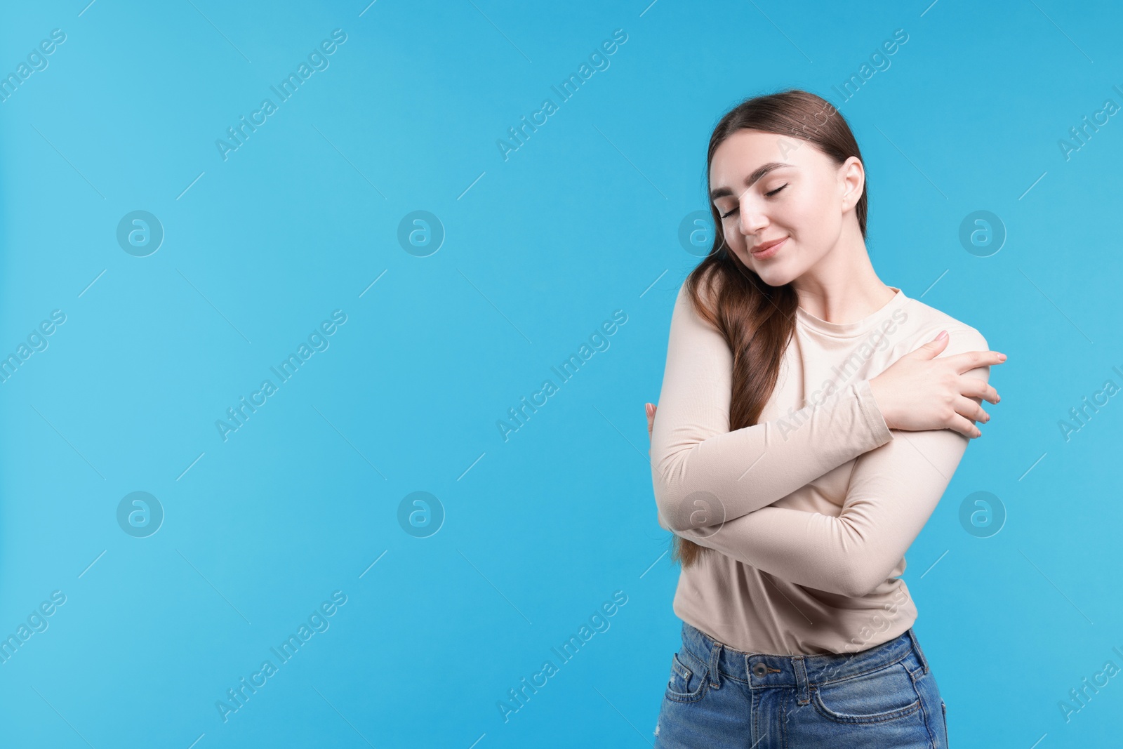 Photo of Charming young woman hugging herself on light blue background. Space for text