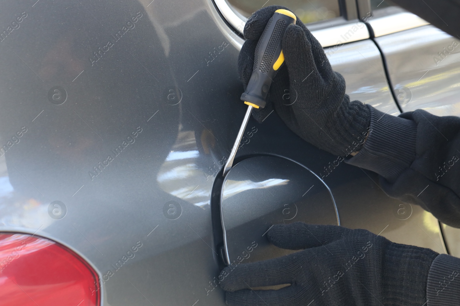 Photo of Thief with screwdriver opening fuel cap, closeup. Car hijacking