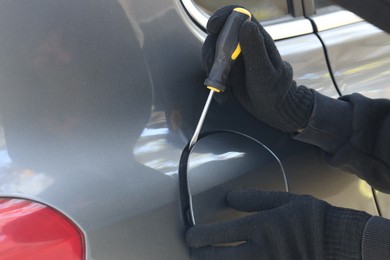 Photo of Thief with screwdriver opening fuel cap, closeup. Car hijacking