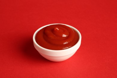 Photo of Tasty ketchup in bowl on red background