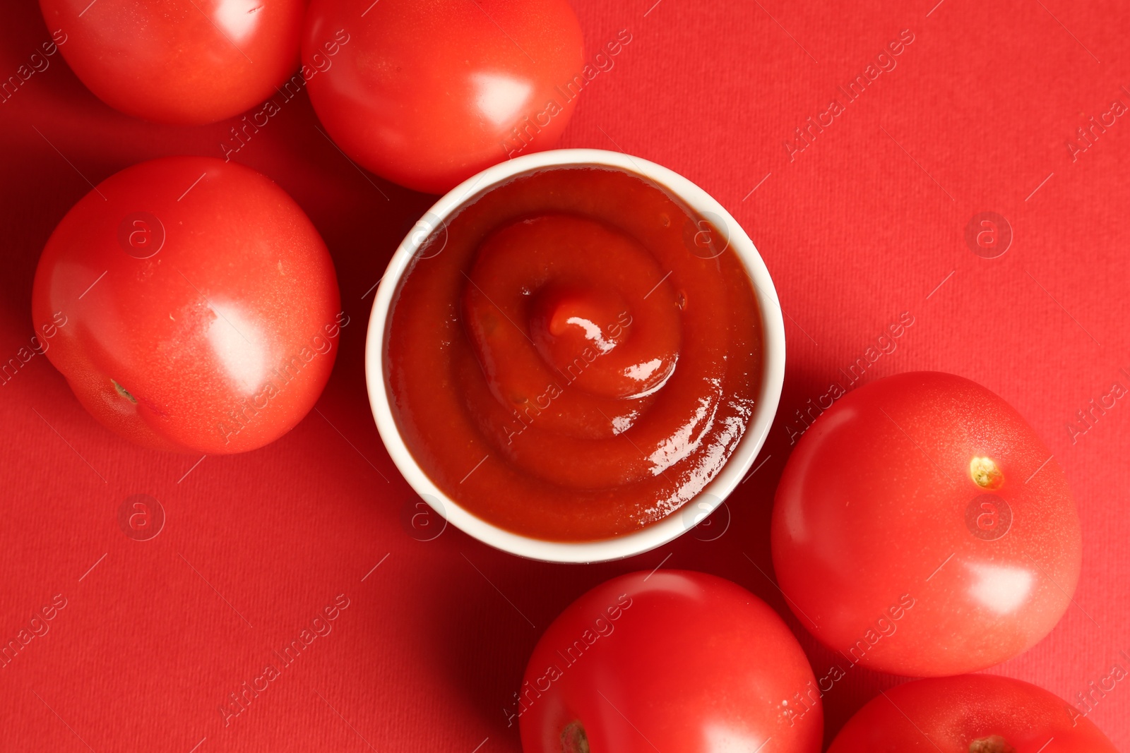 Photo of Ketchup in bowl and fresh tomatoes on red background, flat lay