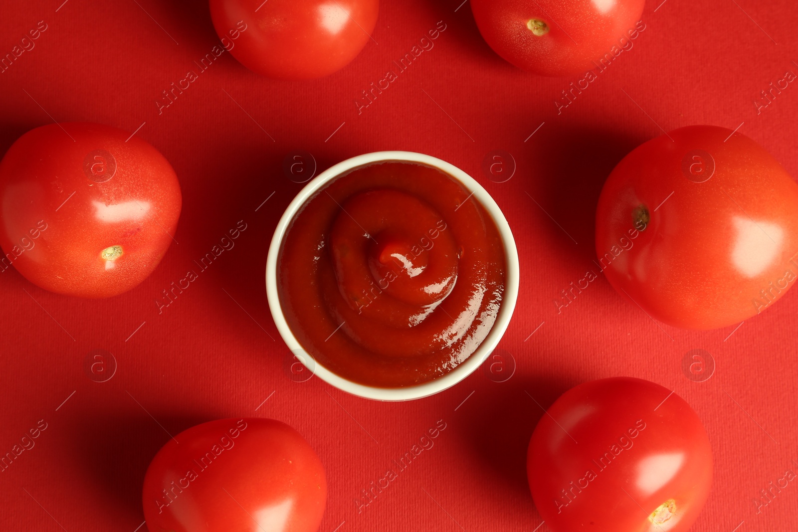 Photo of Ketchup in bowl and fresh tomatoes on red background, flat lay