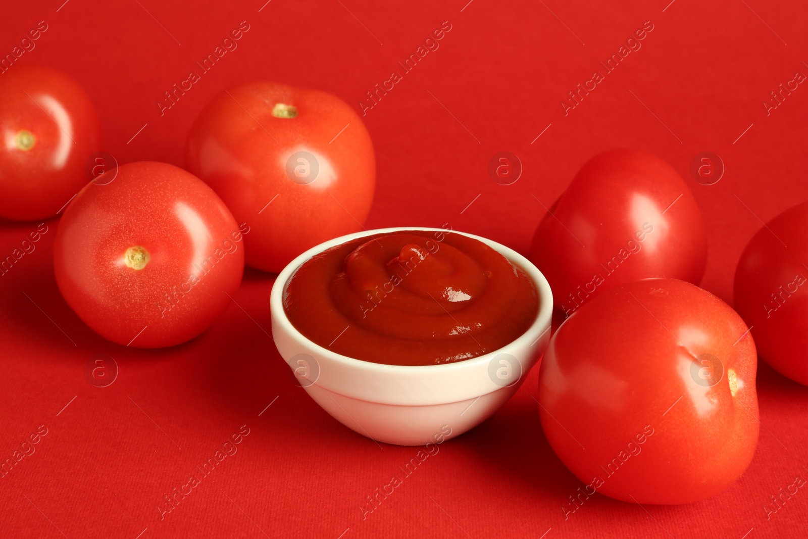 Photo of Ketchup in bowl and fresh tomatoes on red background, closeup