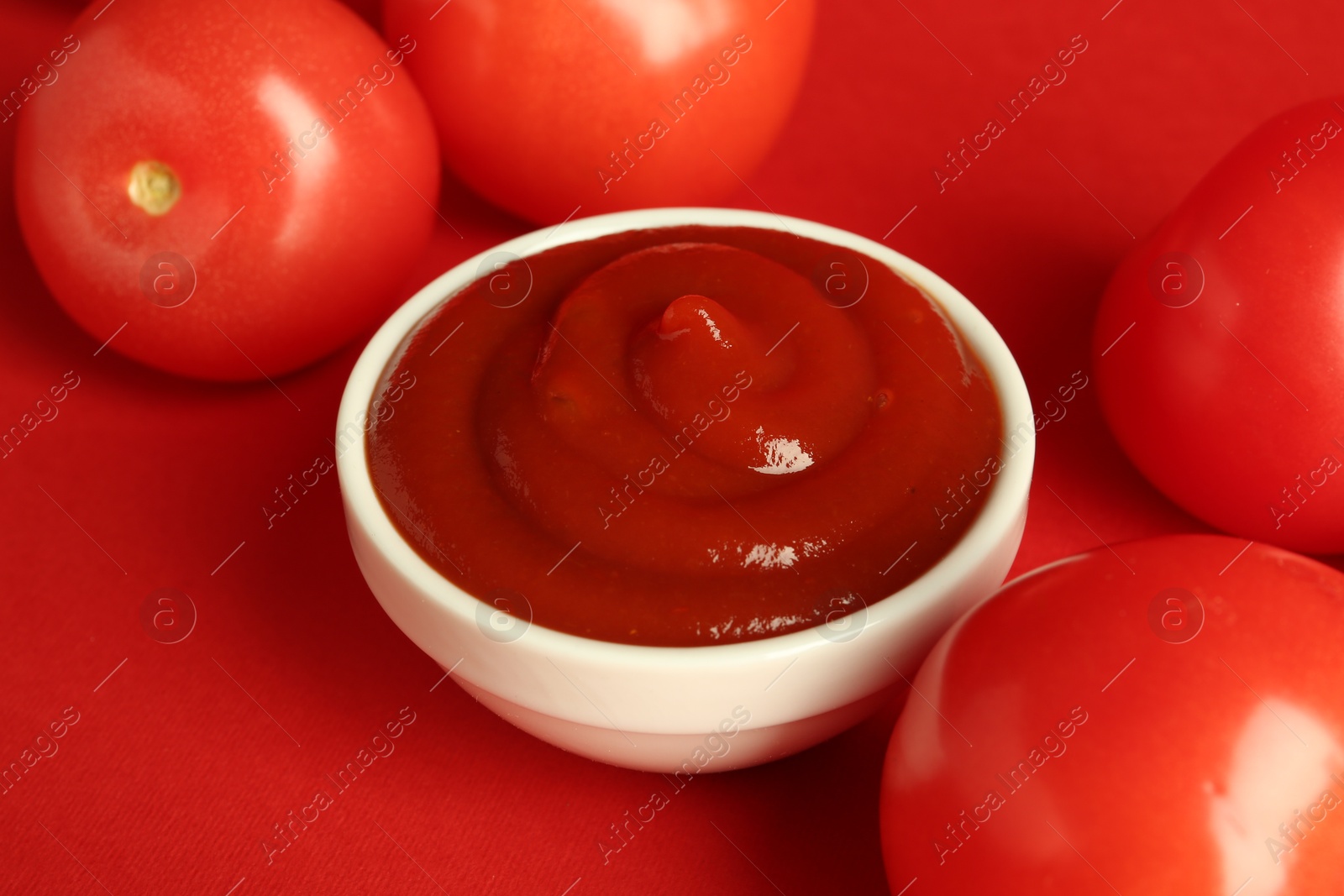 Photo of Ketchup in bowl and fresh tomatoes on red background, closeup