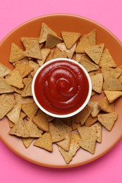 Photo of Ketchup in bowl and pieces of dry bread on pink background, top view