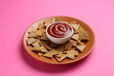 Photo of Ketchup in bowl and pieces of dry bread on pink background