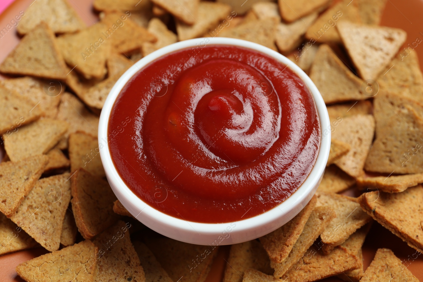 Photo of Ketchup in bowl and pieces of dry bread on plate, closeup