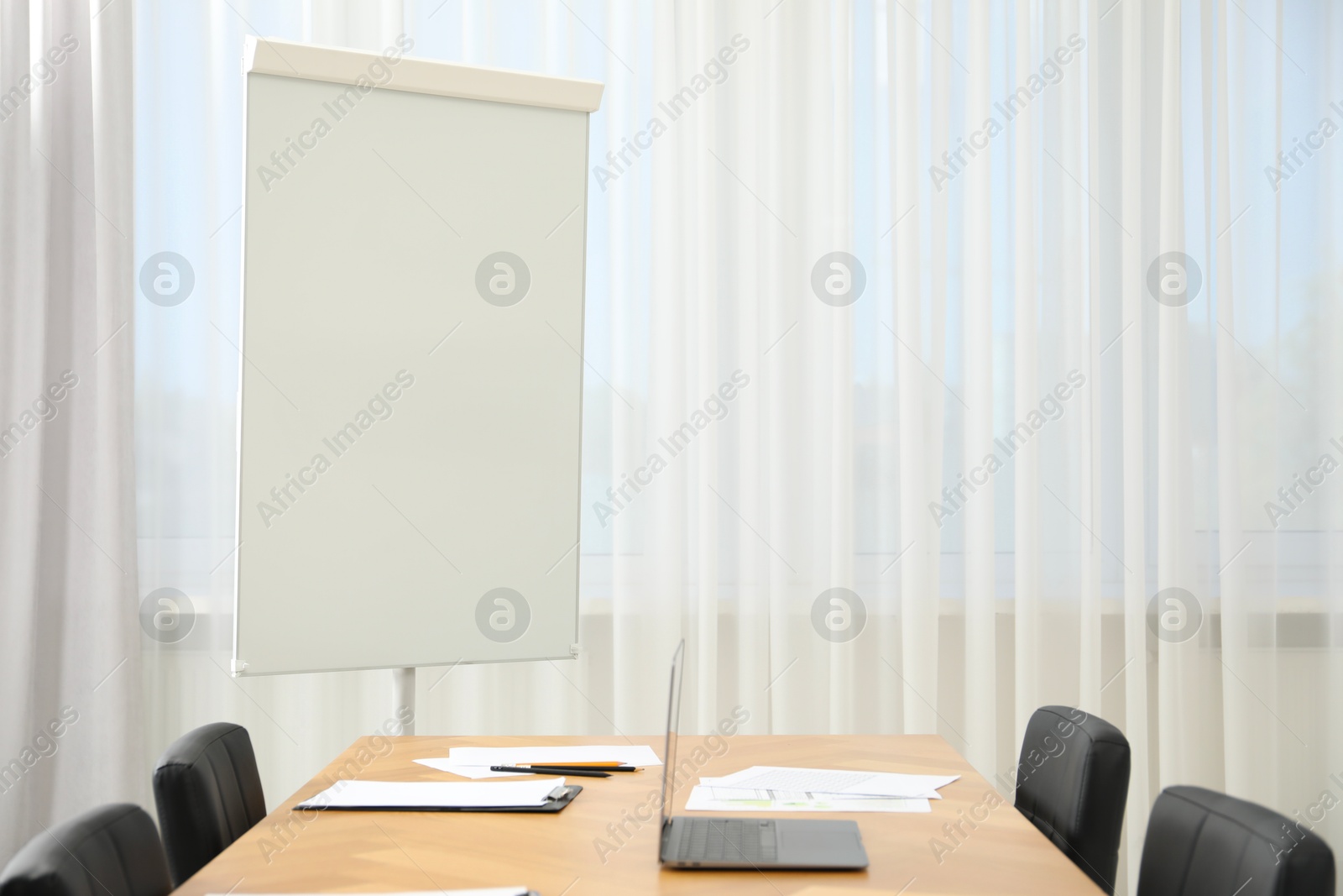 Photo of Flip chart, wooden table and chairs in conference room. Mockup for design