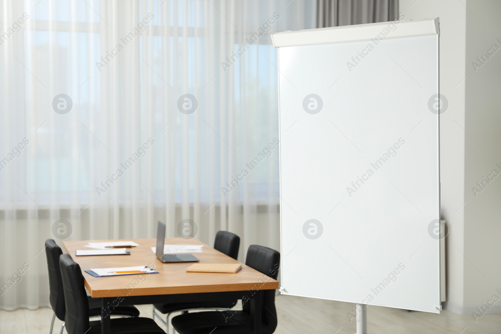 Photo of Flip chart, wooden table and chairs in conference room. Mockup for design