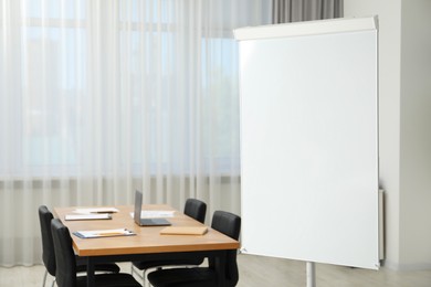 Photo of Flip chart, wooden table and chairs in conference room. Mockup for design