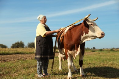 Photo of Senior woman with beautiful cow on pasture