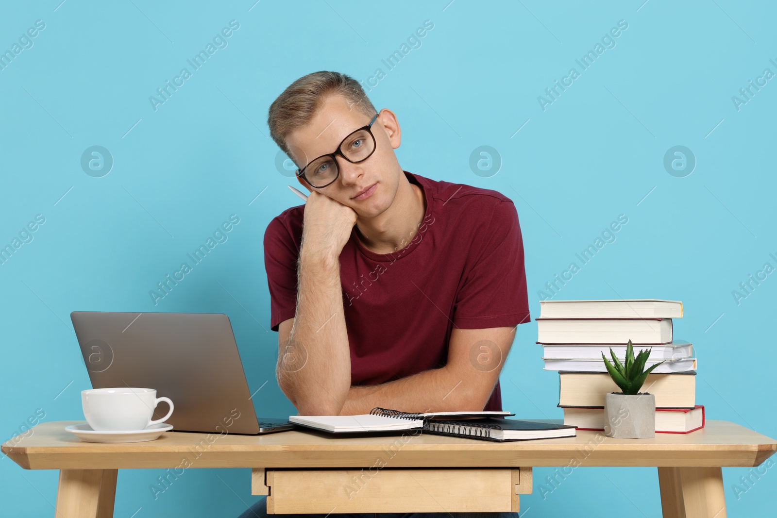 Photo of Preparing for exam. Student with laptop and books at table against light blue background