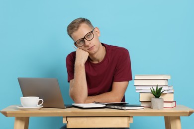 Photo of Preparing for exam. Student with laptop and books at table against light blue background